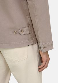 Helles Mauve Jeansjacke mit zwei Knöpfen, einer taillierten Silhouette und leichter Struktur. Kombiniert mit beigefarbenen Hosen, wobei die Taschendetails sichtbar sind.