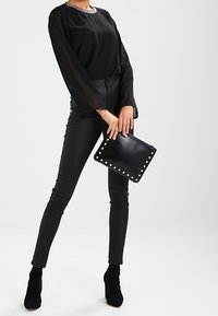 Czarna przezroczysta bluzka z ozdobnym dekoltem, połączona z czarnymi dopasowanymi spodniami. Trzyma czarną torebkę z metalowymi ćwiekami. Uzupełniona czarnymi botkami na obcasie.