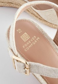 Sandale compensée beige tissée avec bride ajustable, boucle dorée et logo "Forever Comfort" sur semelle intérieure beige, taille 6½/40.