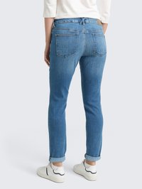 Jean en denim bleu clair avec une coupe slim, ourlets retroussés, deux poches arrière et une taille avec passants. Associés à des baskets blanches.