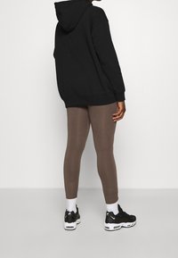 Svart huvtröja, bruna leggings och svarta sportskor med vita detaljer. Huvtröjan har en avslappnad passform och en känguruficka.