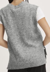 Grauer gestrickter ärmelloser Pullunder mit vertikalen Rippen, weicher Textur und seitlichen Schlitzen, kombiniert mit einem weißen T-Shirt darunter.