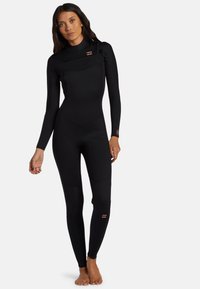 Muta nera con maniche lunghe, design senza cuciture, zip sul petto e gambe aderenti. Presenta un logo rosa sulla manica e sulla coscia.