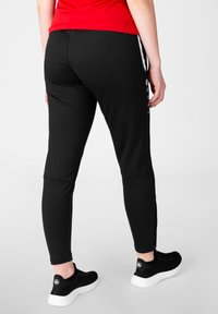Zwarte sportleggings met een aansluitend ontwerp, textuurstof en witte zijkopranden met drukknoopjes. Gecombineerd met zwarte sneakers.