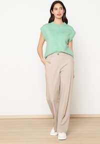 Svetlozeleni kratkoslepi pleteni pulover v kombinaciji s bež širokimi hlačami. Hlače imajo stranske žepe in sprednje zasnovo z gumbom.