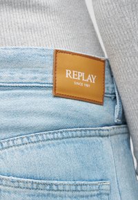 Φωτεινό μπλε τζιν από denim με καφέ δερμάτινη ετικέτα ραμμένη στη μέση που γράφει "REPLAY SINCE 1981."