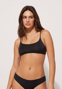 Černá bikiny souprava s jednoduchým, minimalistickým designem s tenkými ramínky a hladkou Texturou. Podprsenka má obdélníkový střih a kalhotky mají střední výšku.