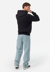 Hanorac negru cu un buzunar mare pe spate, purtat cu blugi largi de culoare albastru deschis. Ținuta include adidași negri cu talpă albă.
