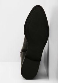 Bottines en cuir noir avec une surface texturée, fermeture éclair sur le côté et une semelle en caoutchouc plate et à motifs. L'intérieur est dépouillé.