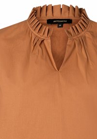 Blouse marron en tissu lisse avec un col légèrement froncé et un décolleté en V. Le design est simple et élégant. Étiquette de taille visible.