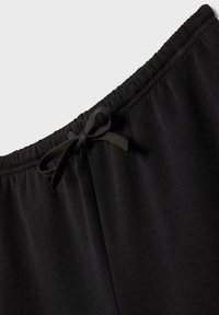 Zwarte broek met elastische tailleband, voorzien van een geperst textuur en een stoffen strik aan de voorkant. Zacht materiaal, ontworpen voor comfort en draaggemak.