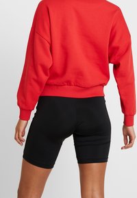Sudadera roja de gran tamaño con puños y dobladillo acanalados, combinada con pantalones cortos negros. La tela parece suave y elástica.