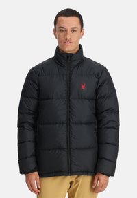 Schwarze Daunenjacke mit hohem Kragen, ausgestattet mit einem roten Spinnenlogo auf der linken Brust, Reißverschluss und gestepptem Design zur Isolierung.