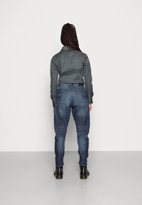 Dunkelgraues Hemd mit Kragen, kombiniert mit blauen Jeans. Das Outfit wird mit schwarzen Stiefeletten abgerundet.