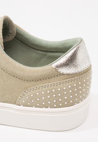 Semišové tenisky v jemném taupe s měkkým zeleným podšívkou. Jsou zdobeny kovovým stříbrným akcentem na patě a bílými hroty po stranách.