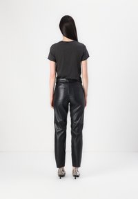 Zwarte leren broek met een rechte snit, voorzien van achterzakken, gecombineerd met een aansluitend grijs T-shirt, gezien vanuit de achterkant.