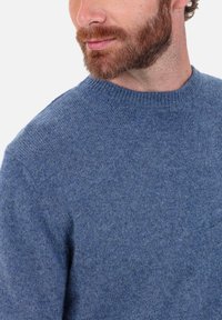 Pull bleu tricoté avec un col ras du cou, fabriqué en matière douce, présentant une texture lisse et des détails côtelés au niveau du col.