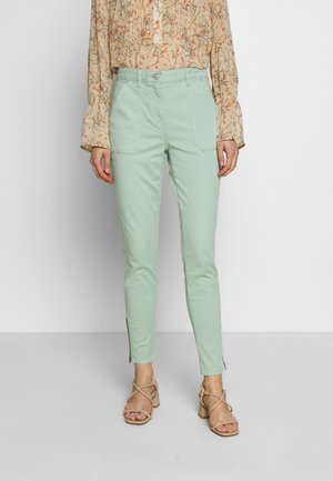 Mintgrønne bukser med sidelommer og lynlåsdetalje ved kanten. Sættet sammen med en mønstret beige bluse.