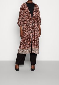Długi, otwarty kimono w kolorze czarnym z misternym różowym wzorem paisley; ma szerokie rękawy i dekoracyjną bordurę u dołu. Noszone z czarnymi spodniami.