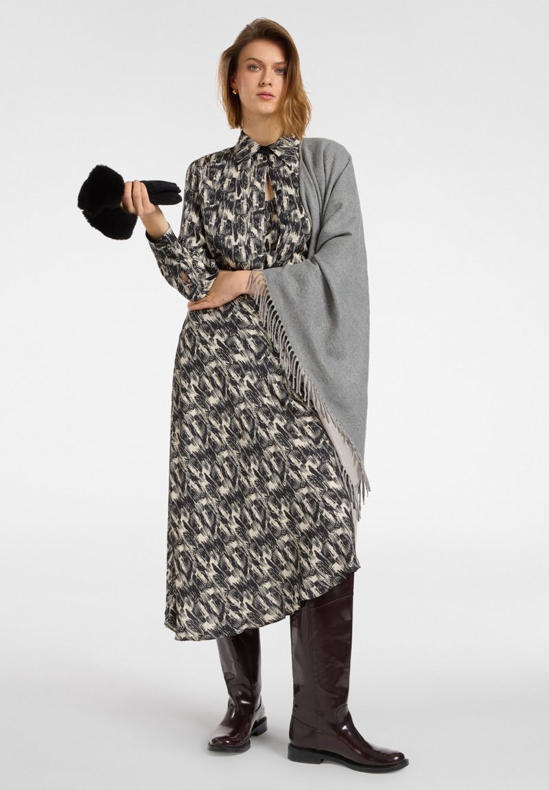 Vestido largo con estampado en crema, negro y gris, con escote en forma de llave, chal gris con flecos y botas de charol burdeos hasta la rodilla.