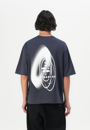 Navyblaues, übergroßes T-Shirt mit einem weißen grafischen Design, das das Wort "OAKLEY" und abstrakte kreisförmige Muster auf der Rückseite zeigt.