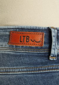 Traperice s smešnim kožnim oznakom "LTB", plavim šavovima, standardnim pojasom i klasičnim dizajnom s pet džepova.