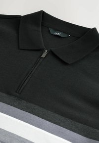 Černé polo tričko na zip s texturovaným límcem, které má horizontální pruhy v černé, šedé a bílé barvě po celém trupu.
