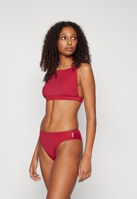 Ensemble bikini rouge comprenant un haut sans manches avec un col rond et un bas taille haute assorti, fabriqué dans un matériau lisse et extensible.