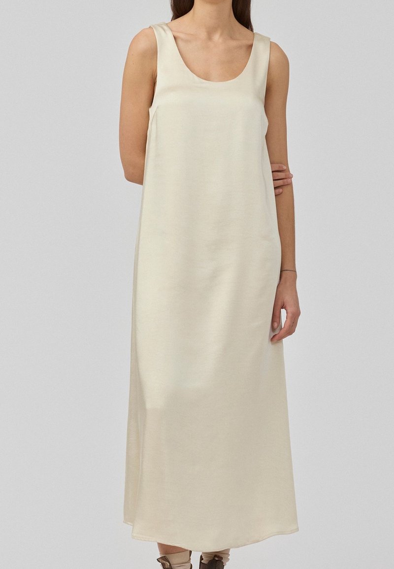 Robe maxi sans manches en tissu beige clair, dotée d'un décolleté en arrondi et d'une silhouette ample, avec une texture lisse et mate.