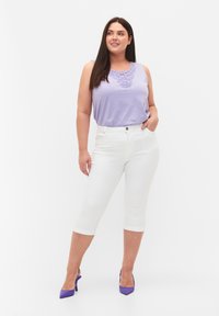 Top sin mangas de color lila con cuello bordado, combinado con jeans blancos recortados y zapatos de tacón altos morados sobre un fondo liso.