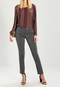 Top a maniche lunghe bordeaux a fantasia abbinato a pantaloni stretti grigi con texture e sandali neri con tacco alto, insieme a una piccola borsa a tracolla.