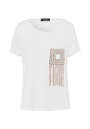 Weißes T-Shirt mit Rundhalsausschnitt und kurzen Ärmeln. Mit einer quadratischen Häkel-Tasche mit Fransen in Beige und Weiß.