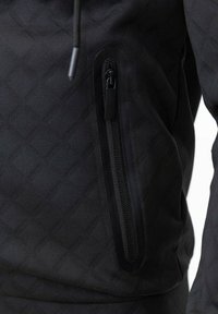 Veste noire avec un motif texturé, poche zippée avec un bord contrasté et une capuche à cordon. Tissu doux avec un design athlétique.