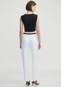 Zwarte crop top met korte mouwen, gecombineerd met witte nauwsluitende broek met een elastische tailleband en achterzakken, gedragen met zwarte hakken.