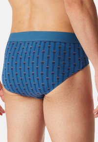 Blauwe gebloemde slips met een zachte tailleband. Kenmerkt zich door verticale strepen en kleine horizontale accenten voor detail. De stof lijkt soepel en rekbaar te zijn.
