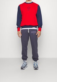 Sweat-shirt rouge et bleu marine à col rond, avec logo Nike et manches longues ; assorti à un pantalon de jogging gris portant le logo "Liverpool FC" et des poignets élastiques.