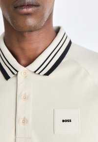 Poloshirt in beige katoen met een zwart-wit gestreepte kraag, knoopsluiting en een vierkante logopatch met de merknaam "BOSS".
