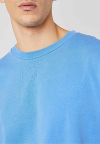 Svetlo modra bombažna majica ima okroglo izrezovanje in kratke rokave, z gladko teksturo in minimalnim šivnim detajlom.