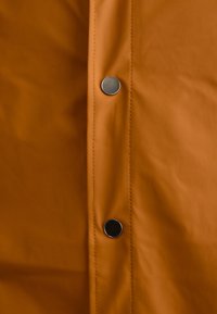 Țesătură impermeabilă portocalie cu o textură netedă, având două capse metalice pe față. Design minimalist cu cusături vizibile.