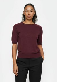 Burgundia lühikeste varrukatega kampsun soonilise tekstuuri ja ümarkaelusega, millele on kombineeritud mustad püksid, modell kannab valge tausta ees.