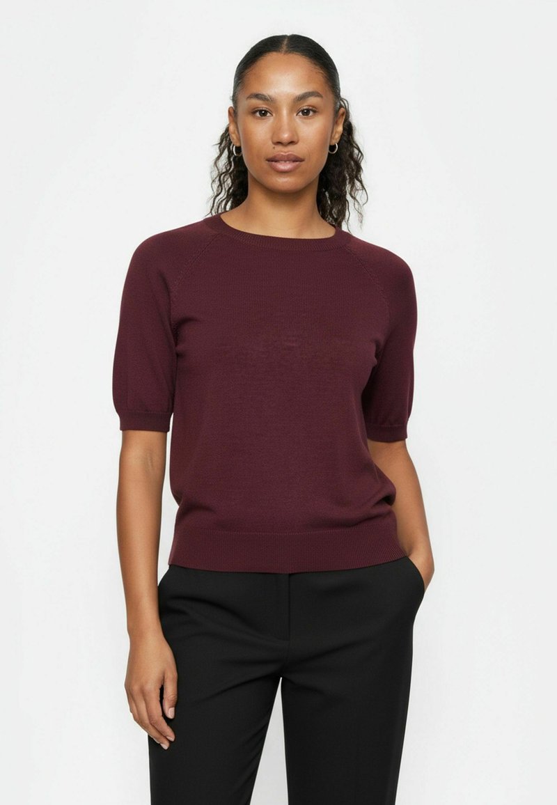 Burgundia lühikeste varrukatega kampsun soonilise tekstuuri ja ümarkaelusega, millele on kombineeritud mustad püksid, modell kannab valge tausta ees.