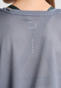 Grå mesh träningslinne med små hål för andningsförmåga, rund halsringning och diskret ryggdetalj med präglat mönster.