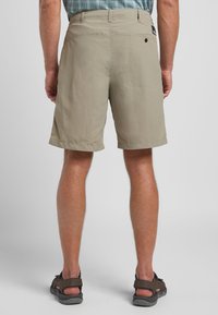 Pantaloni corti color khaki realizzati in tessuto leggero, con tasca posteriore con chiusura a bottone e vita piatta. Indossati con sandali marroni.