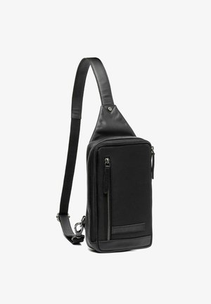 Zwarte schoudertas van een combinatie van textuurleer en stof. Het heeft een ritsvak, een verstelbare schouderband en een slank ontwerp.