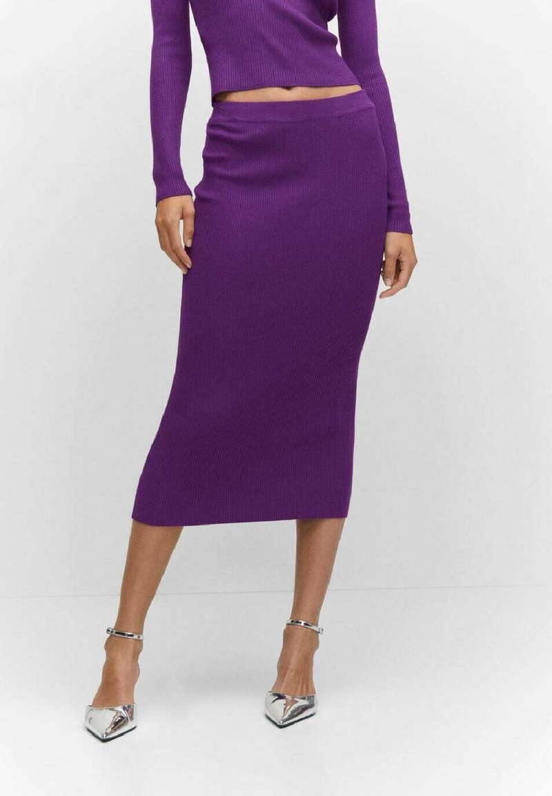 Femme portant une jupe midi en tricot côtelé violette et un haut à manches longues assorti avec des escarpins argentés à bout pointu sur un fond blanc.