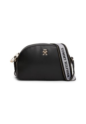 Schwarze halbkreisförmige Crossbody-Tasche mit goldenem Logo und verstellbarem weißen Riemen mit „Tommy Hilfiger“-Schriftzug und schwarzen Streifen.