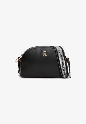 Czarna półokrągła torebka na ramię ze złotym logo i regulowanym białym paskiem z napisem „Tommy Hilfiger” oraz czarnymi paskami.