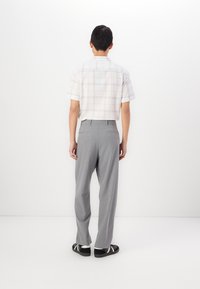 Chemise blanche à manches courtes avec un motif à carreaux, associée à un pantalon gris ample et des baskets noires avec des accents blancs, vue de dos.