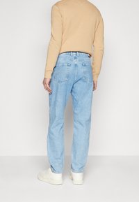 Vaaleansiniset farkut suoralla lahkeella, joissa on takataskut ja korkea vyötärö, yhdistettynä beigeen neulepaitaan ja valkoisiin lenkkareihin.