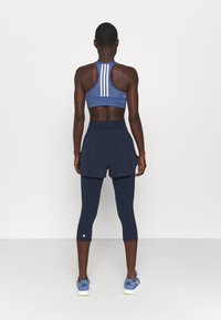 Námořnický sportovní outfit obsahující sportovní podprsenku s racerbackem a bílými pruhy, doplněný námořnickými šortkami přes zkrácené legíny a modré sportovní boty.